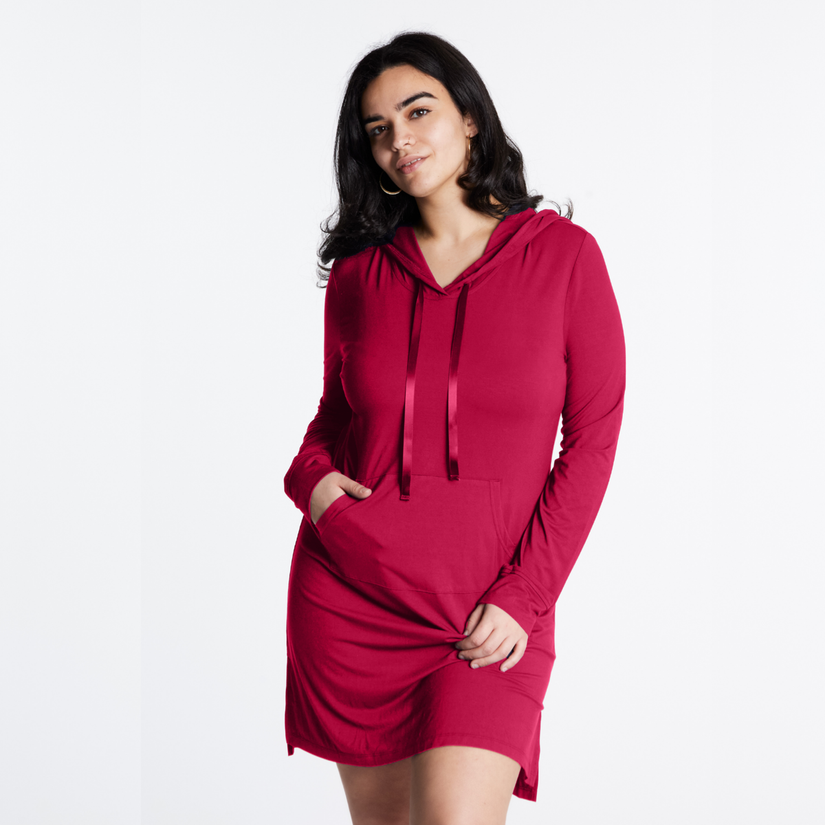 A woman modeling a long-sleeve hooded mini dress in a deep raspberry pink color, standing against a plain white studio background.