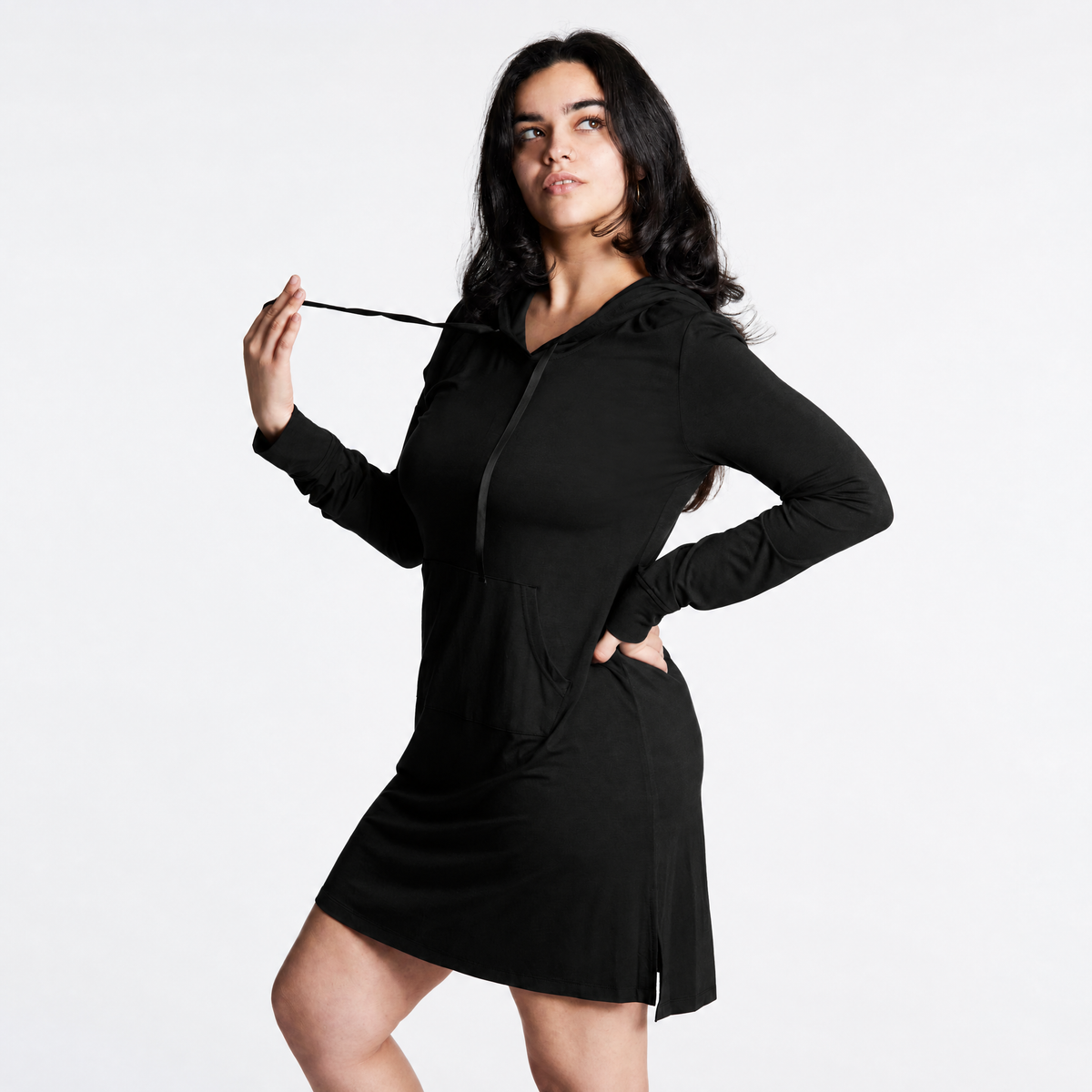 A woman modeling a long-sleeve hooded mini dress in black (Midnight), standing against a plain white studio background.