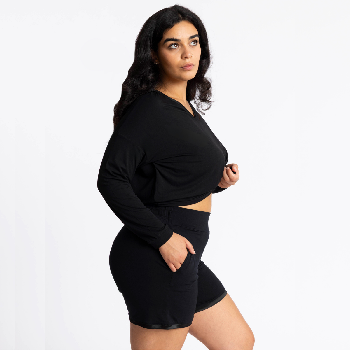 A woman modeling a black long-sleeve Tuxedo-Striped top and matching black lounge shorts with pockets against a plain white studio background.